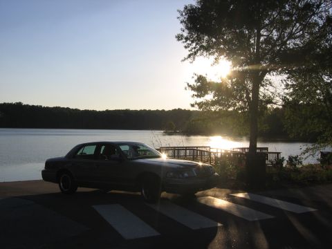 2000 Ford Crown Victoria - A sedan is parked near a lake during sunset, with the sun glinting off the water.
