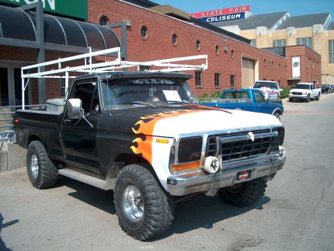 1978 Ford Bronco - Modified pickup truck with flames and ladder rack parked outside a coliseum.