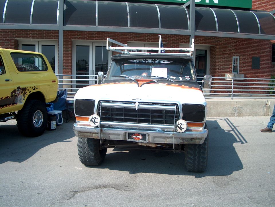 Front view of a lifted 1970s Ford F-Series truck with custom paint. A yellow Ford Bronco is parked to the left