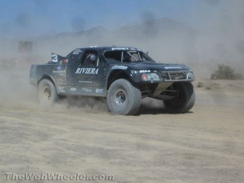 1990 Ford Bronco - black off-road race truck number 3 lettered RIVIERA races through a dusty desert course.