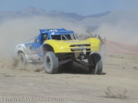 1990 Ford Bronco - yellow off-road race truck and a blue number 40 truck race side by side through the dusty desert.