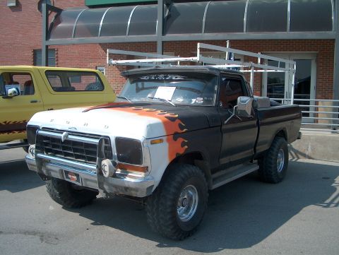 1978 Ford Bronco - This modified Ford pickup truck features a custom paint job and a roof rack, parked next to a yellow SUV.