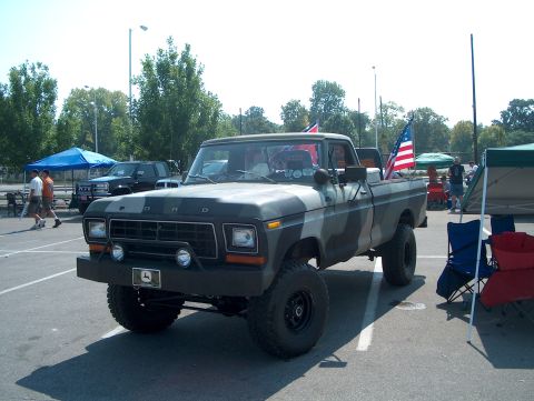 1978 Ford Bronco - A camouflaged 1978 Ford pickup truck is parked outdoors with American flags visible.