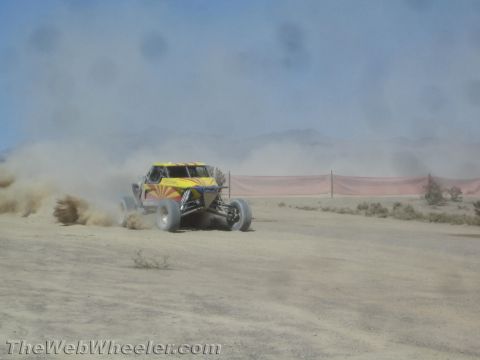 1990 Ford Bronco - yellow off-road race buggy with red sunburst graphics powers through a dusty desert course.