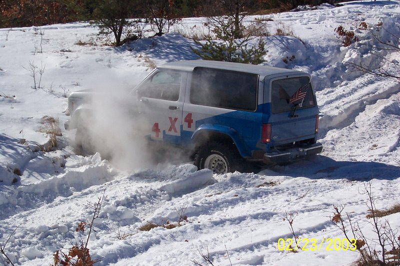 White and blue Ford Bronco II with red 4x4 graphics driving in snow, kicking up dust