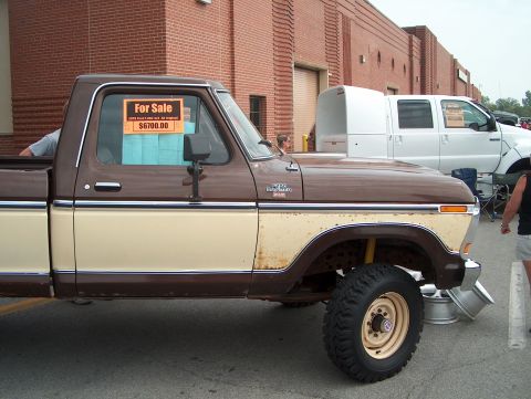 1978 Ford Bronco - A two-tone pickup truck is parked next to a white truck, with a building in the background.