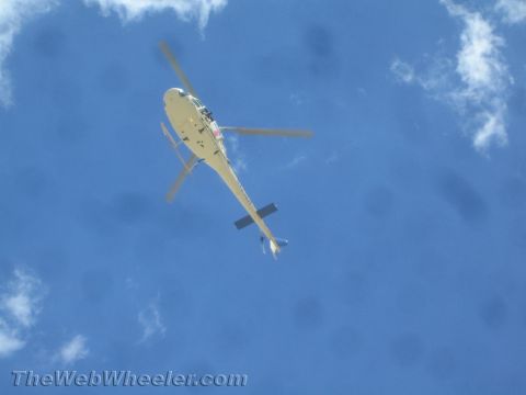 1990 Ford Bronco - light-colored helicopter flies overhead against a blue sky with scattered clouds.
