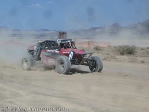 1990 Ford Bronco - red off-road race buggy fitted with a roof light bar speeds along a dusty desert course.
