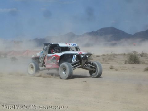 1990 Ford Bronco - red and white off-road race buggy marked 136 speeds along a dusty desert course before distant mountains.