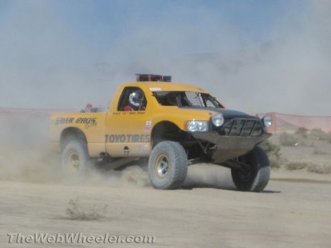 1990 Ford Bronco - yellow off-road race truck lettered with Greer Bros and Toyo Tires speeds across a dusty desert course.