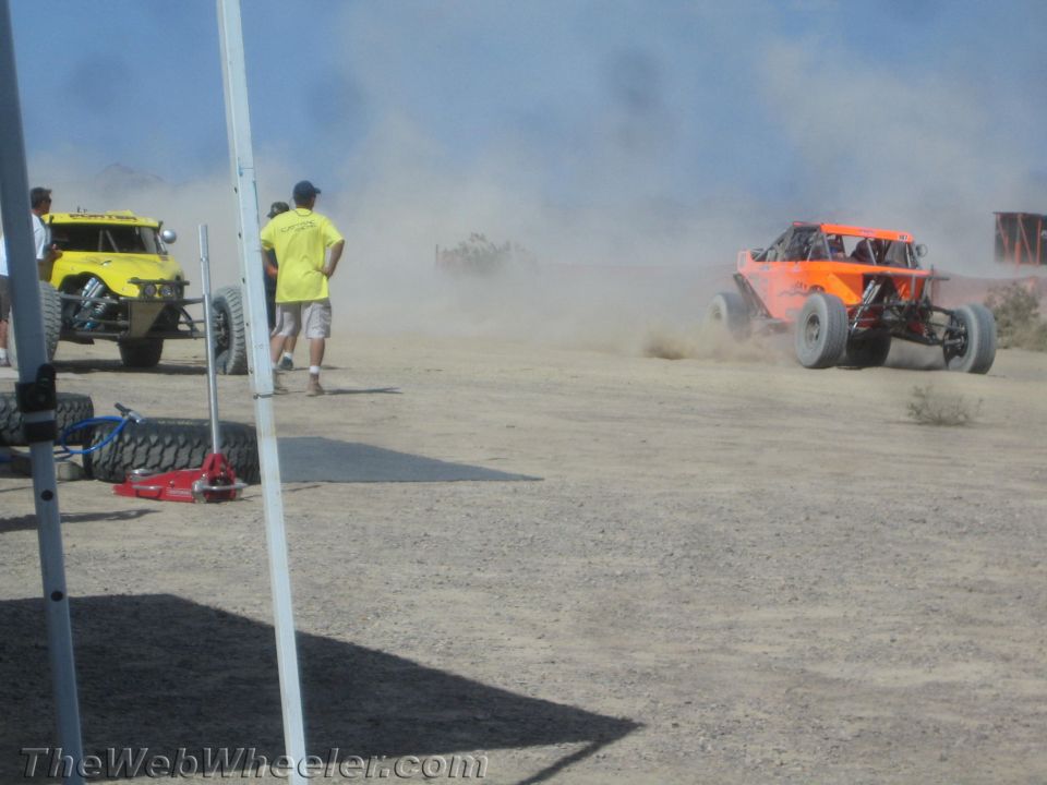 Off-road buggies racing past a pit area with spectators