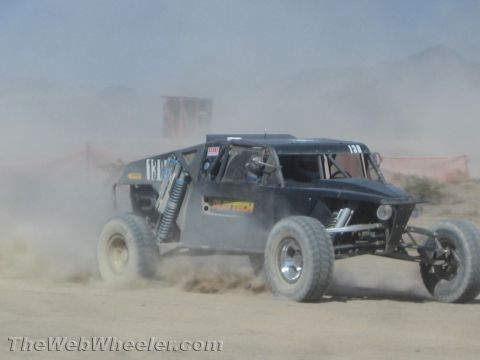 1990 Ford Bronco - dark gray off-road race buggy with Baytech lettering speeds through heavy dust on a desert course.