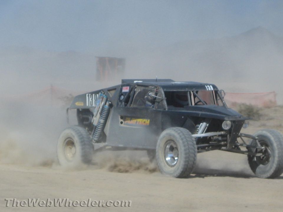 Dark gray off-road buggy racing through heavy desert dust