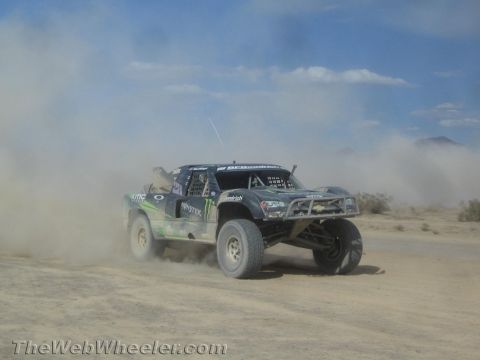 1990 Ford Bronco - dark off-road race truck with Monster and Oakley livery powers through thick dust in the open desert.
