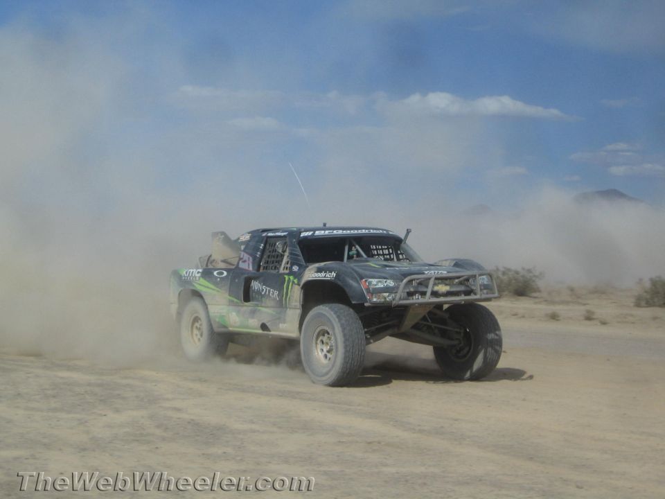 Dark Monster-liveried off-road race truck racing through heavy desert dust