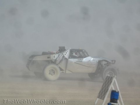 1990 Ford Bronco - tan off-road race truck marked 0 is almost obscured by a dense cloud of dust near a course marker.