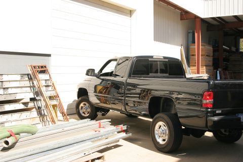 2002 Dodge 2500 - A black Dodge pickup truck is parked outside a building with various construction materials stacked around it.