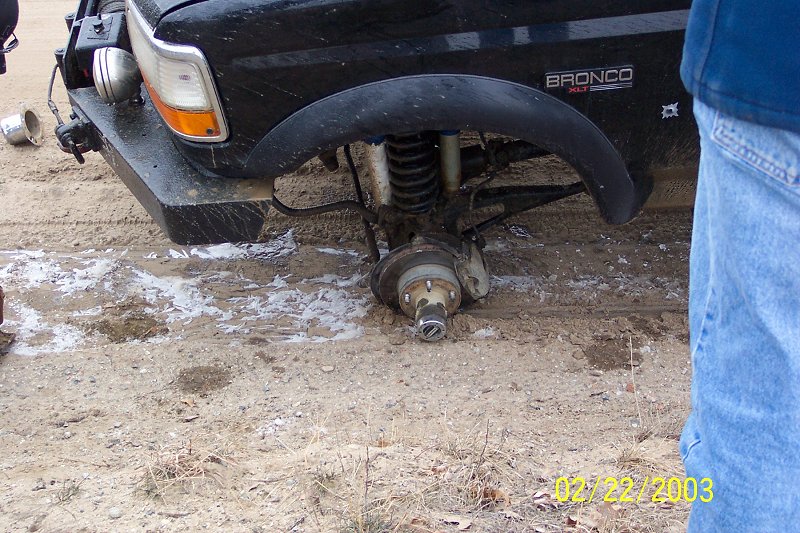 Front coil-spring suspension and exposed hub of a black Ford Bronco jacked up outdoors