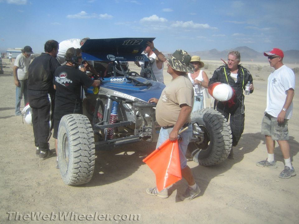 Crew and spectators around a blue and silver off-road buggy number 102 in the pits
