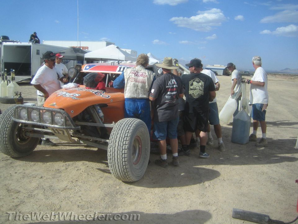 Crew gathered around an orange off-road buggy with light bar in a desert pit area