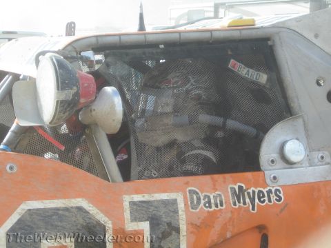 1990 Ford Bronco - close-up of an orange off-road race vehicle's screened engine bay shows a shock reservoir, "BEARD" seat tag, and "Dan Myers" lettering.