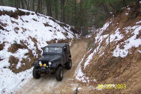 1978 Ford Bronco - Jeep CJ-7 navigates a challenging winter trail with snow on the banks.