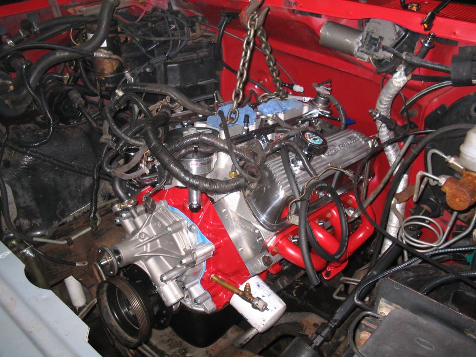 Engine being lifted into place, showing red block and chrome valve covers