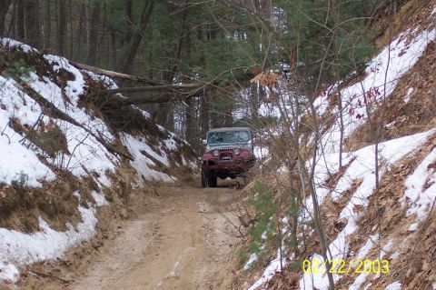 1978 Ford Bronco - A Jeep Wrangler navigates a narrow, wooded trail with snow on the banks.