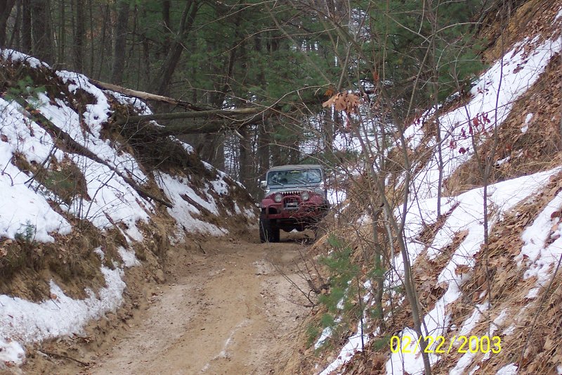 Jeep Wrangler driving on a muddy, snowy trail through a forest