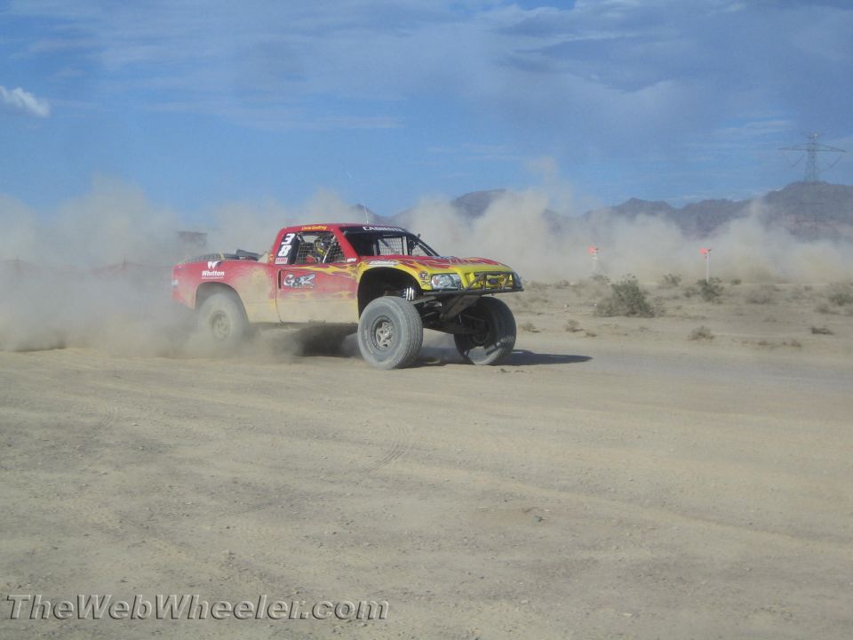 Red and yellow off-road race truck cornering hard in dust in the desert