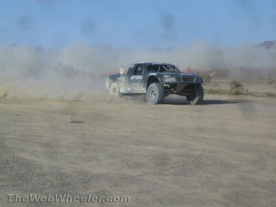 Dark off-road race truck with Riviera livery sliding through dust in the desert