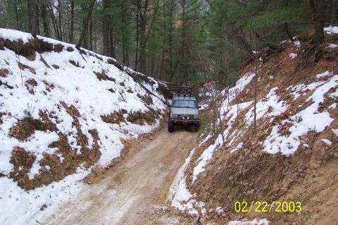 1978 Ford Bronco - A silver SUV navigates a dirt road through a snow-covered forest.