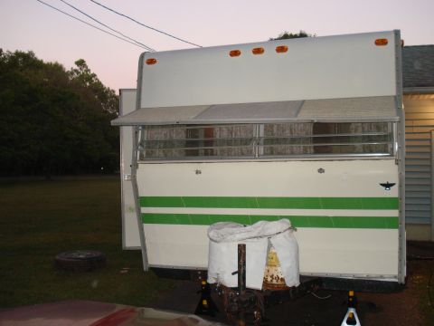 1994 Ford Bronco - A travel trailer with green stripes and an awning is parked outside at dusk. A spare tire is visible on the ground.