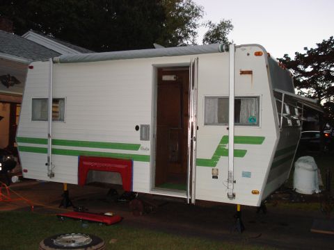 1994 Ford Bronco - A white camper trailer with green stripes is parked outdoors, with its door open and supported by stabilizing jacks.