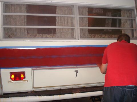 1994 Ford Bronco - A person in a red shirt paints a red stripe on the side of a camper, with blue tape marking the edges.