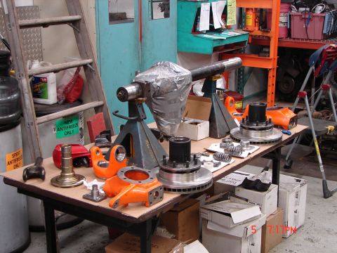 1989 Ford Bronco - Various Dana 60 front axle parts are laid out on a table in a workshop setting.