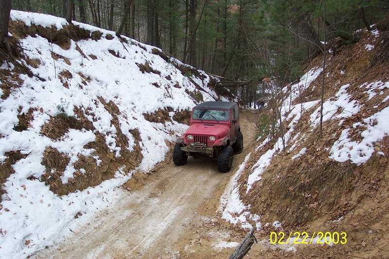 Red Jeep Wrangler with large tires on a muddy, snow-dusted trail