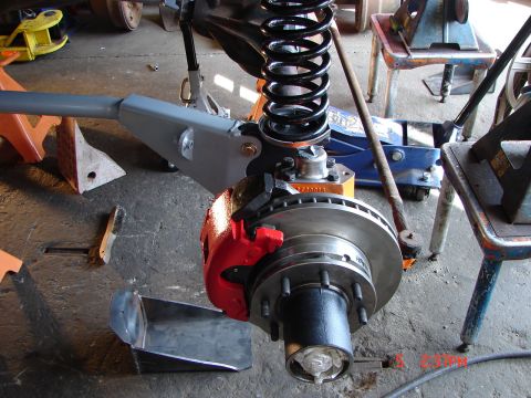 1989 Ford Bronco - Close-up view of a Dana 60 front axle assembly, a red brake caliper and a large coil spring, likely undergoing maintenance or upgrade.