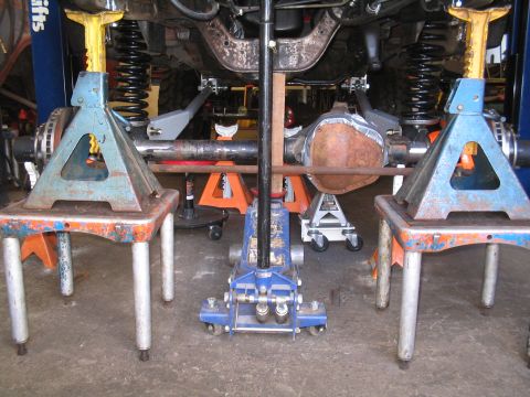 1989 Ford Bronco - The underside of a vehicle is shown, with the rear axle and suspension system elevated on jack stands.