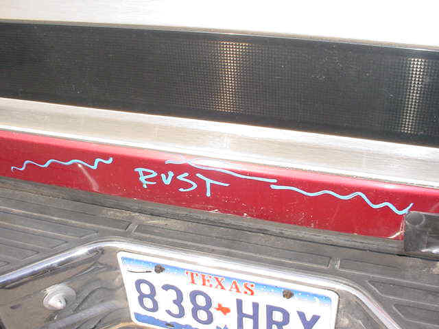 Rear bumper of a vehicle with 'RUST' written on it in blue marker. Texas license plate visible