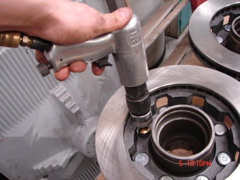 1989 Ford Bronco - Close-up of a mechanic using an impact wrench on a vehicle's brake rotor assembly.