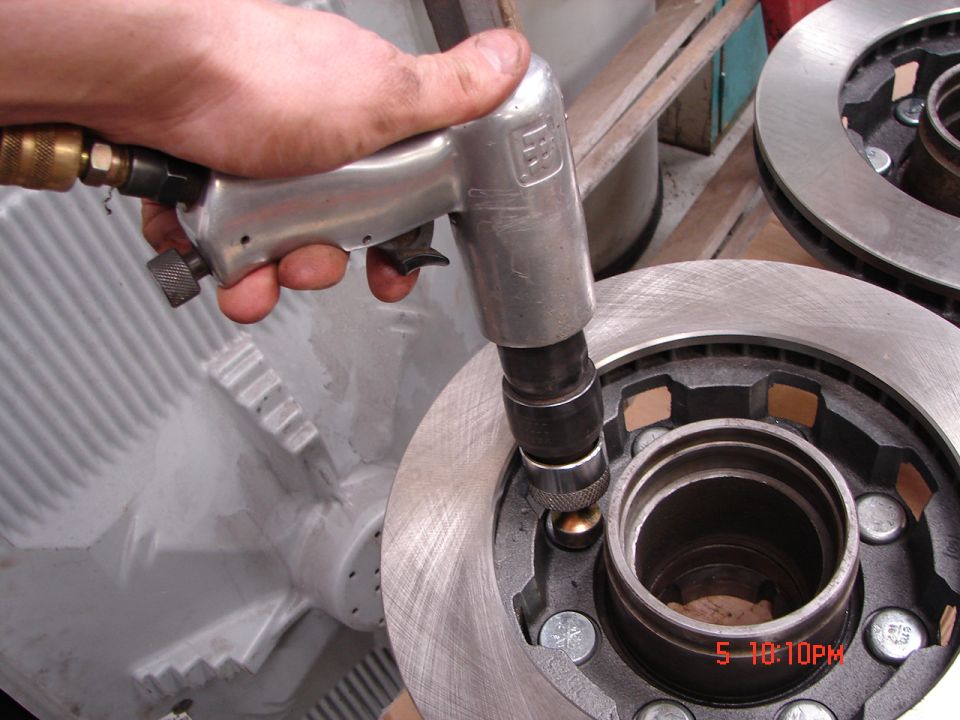 Impact wrench tightening lug nuts on a brake rotor assembly. Another rotor is visible in the background