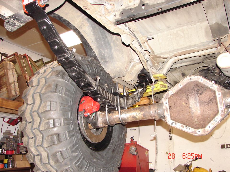 close-up of a large off-road tire, leaf springs, and a heavy-duty rear axle with red brake calipers