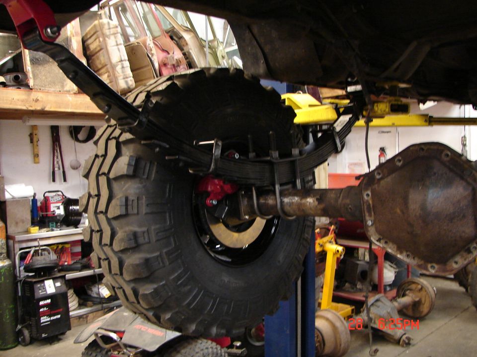 Rear axle assembly with large tire and leaf springs, red brake caliper visible