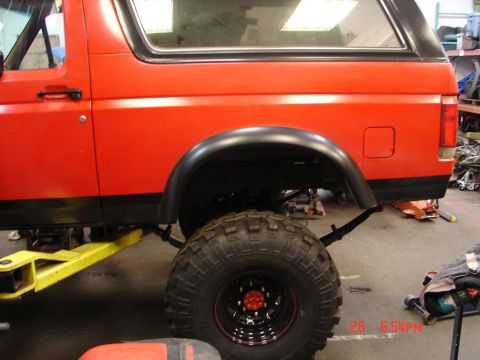 1989 Ford Bronco - Side view of a red SUV with off-road tires, partially raised on a yellow hydraulic lift.
