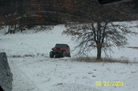 1978 Ford Bronco - A red Jeep Wrangler navigates through a snow-covered landscape with a bare tree nearby.
