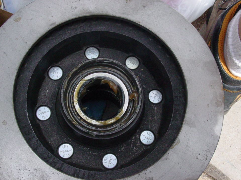 Wheel hub with grease and lug bolts next to a brake rotor. Shoe visible at top right