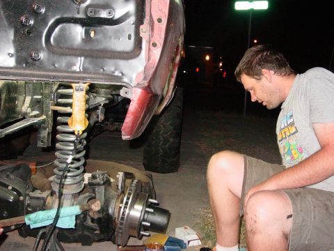 1979 Ford Bronco - A man works on the front suspension of a vehicle at night, with streetlights in the background.