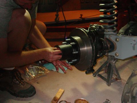 1979 Ford Bronco - A person works on a front axle assembly, including the hub and brake rotor, supported by jack stands.