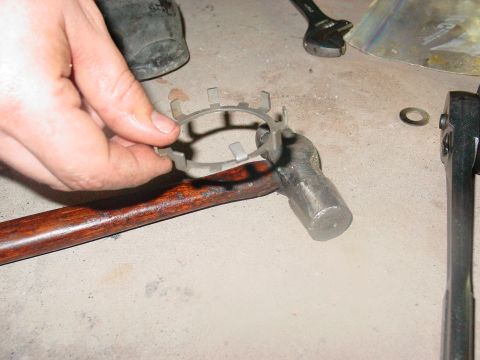 1979 Ford Bronco - A metal part is held over a hammer, with tools and a washer visible on the concrete floor.